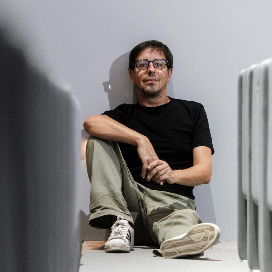 Homem de óculos e vestes casuais posa sentado no chão