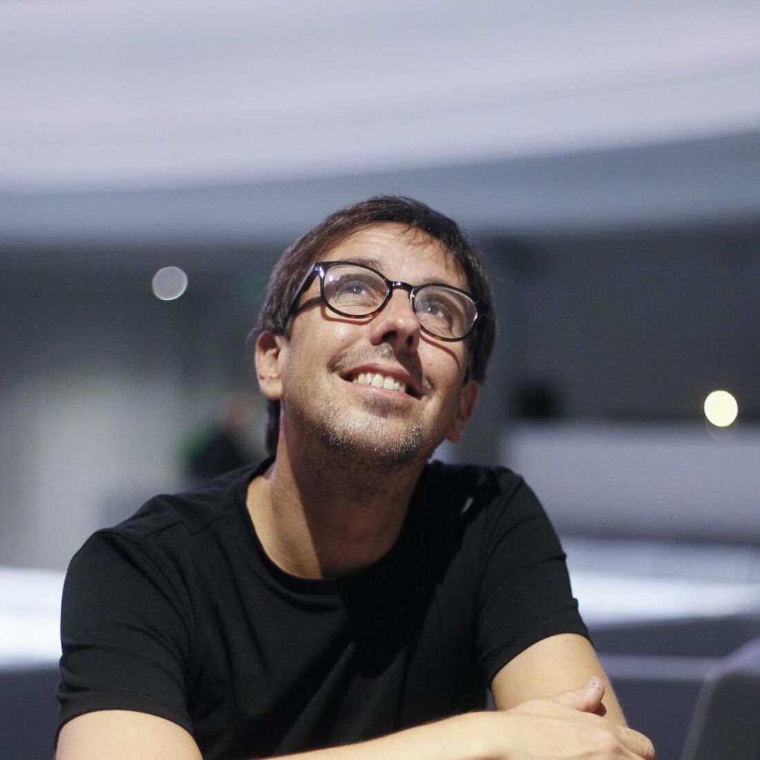 Homem de óculos sorri e olha para cima, sentado numa cadeira