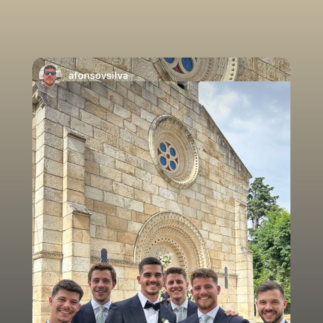 Grupo de homens em fatos elegantes posa em frente a uma igreja de pedra