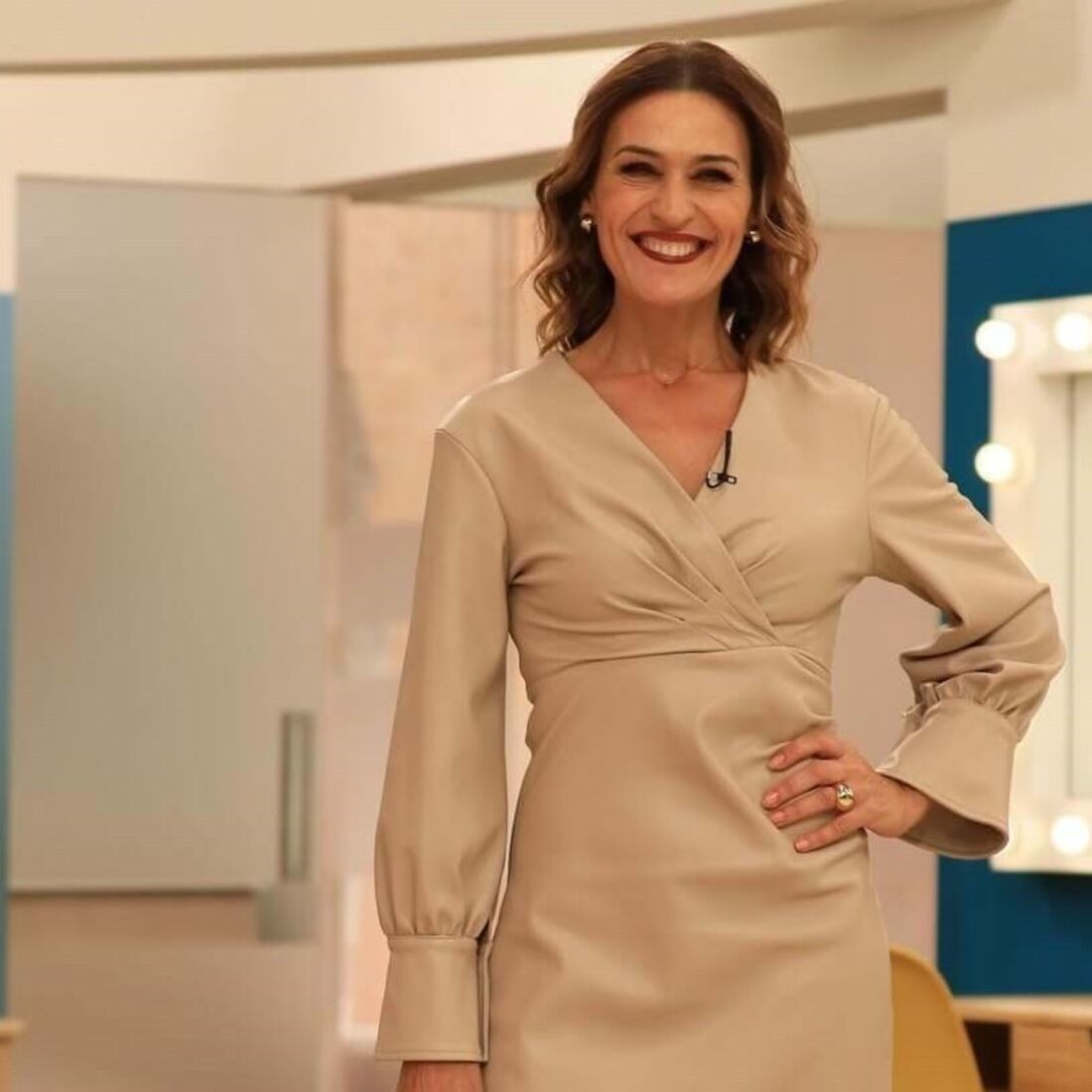 Mulher sorri com vestido bege em estúdio