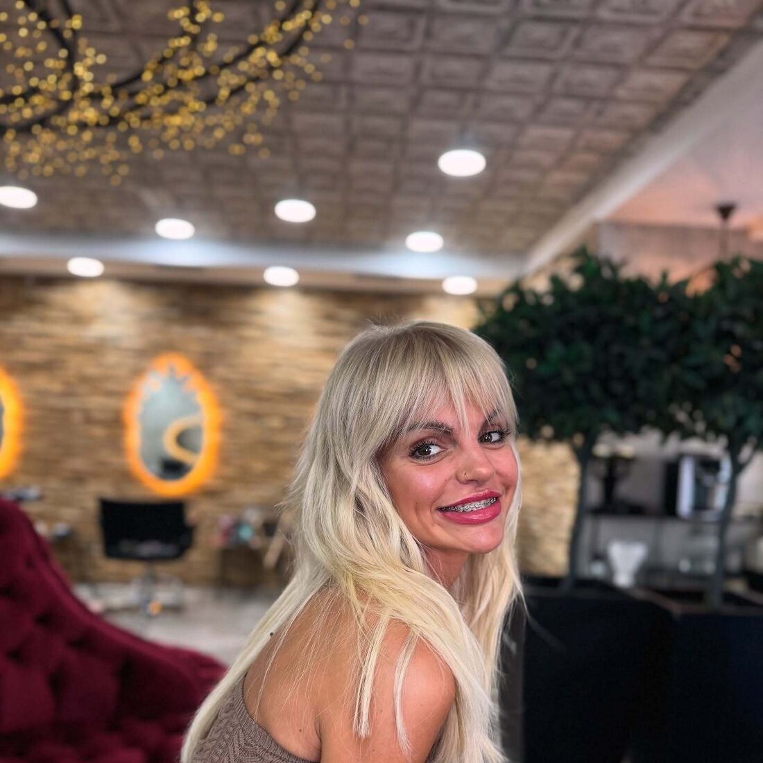 Mulher sorri com aparelho ortodôntico e piercing no nariz num salão