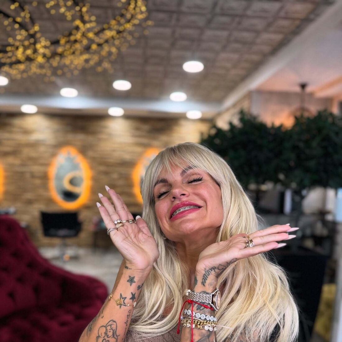 Mulher sorri com aparelho nos dentes, exibe tatuagens e acessórios