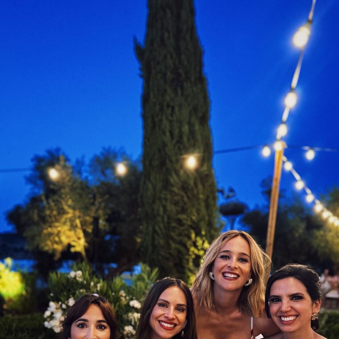 Quatro mulheres sorriem num evento ao ar livre