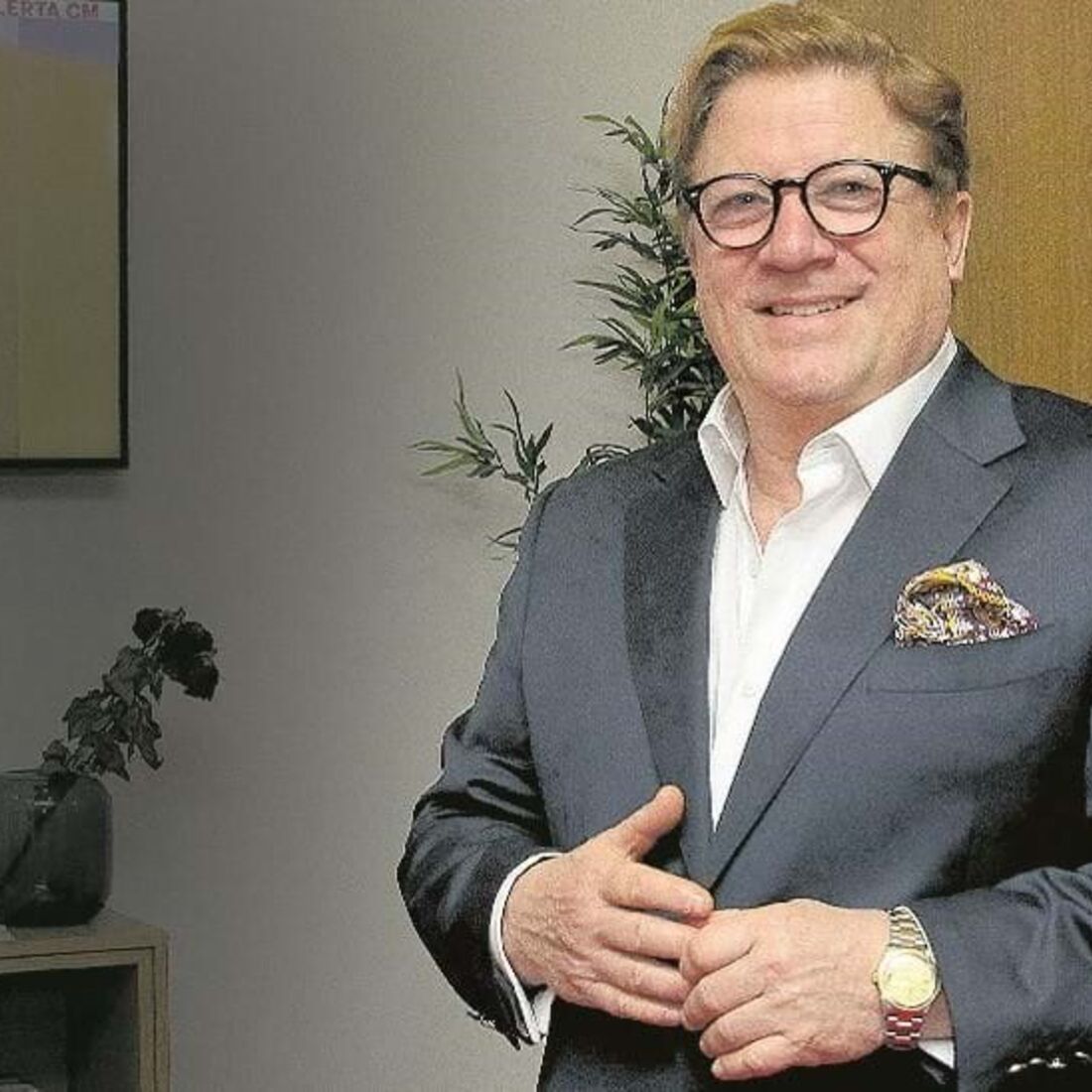 Um homem de óculos e fato posa para a câmara