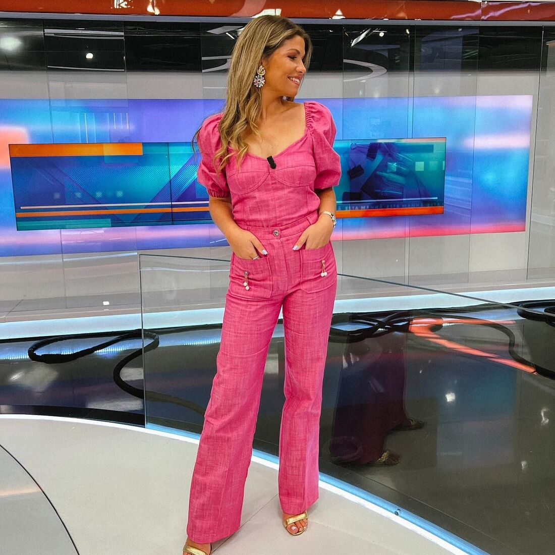 Mulher sorri num estúdio de televisão com um fato rosa