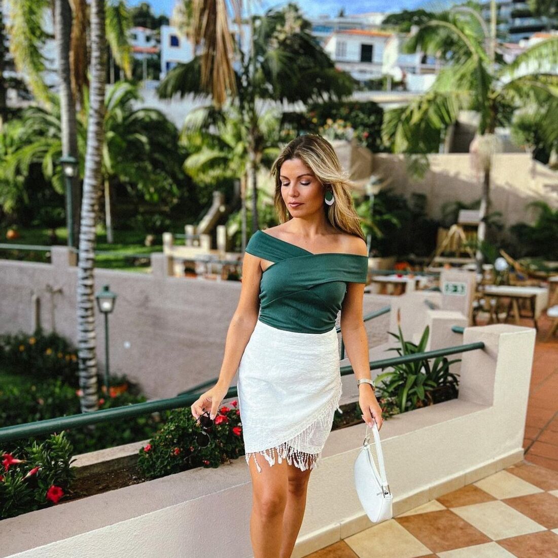 Mulher posa com saia branca e top verde num espaço exterior com palmeiras