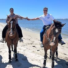 Hugo e Raquel desfrutam de passeio a cavalo na praia sob céu azul.