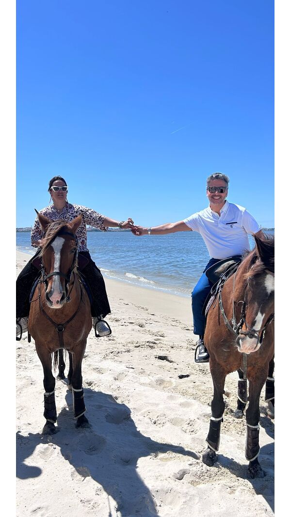 Pessoas desfrutam de passeio a cavalo na praia sob céu azul.