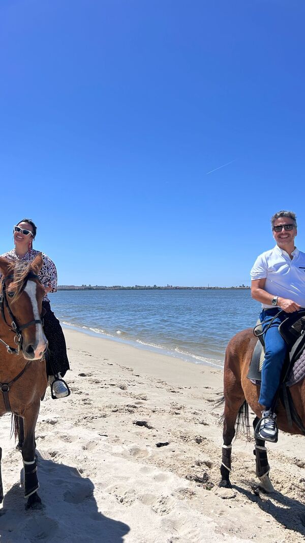 Pessoas aproveitam passeio a cavalo na praia com céu azul