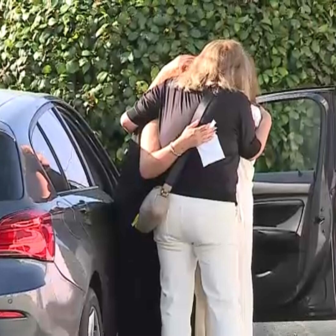 Duas mulheres abraçam-se junto a um carro, mostrando apoio em momento difícil