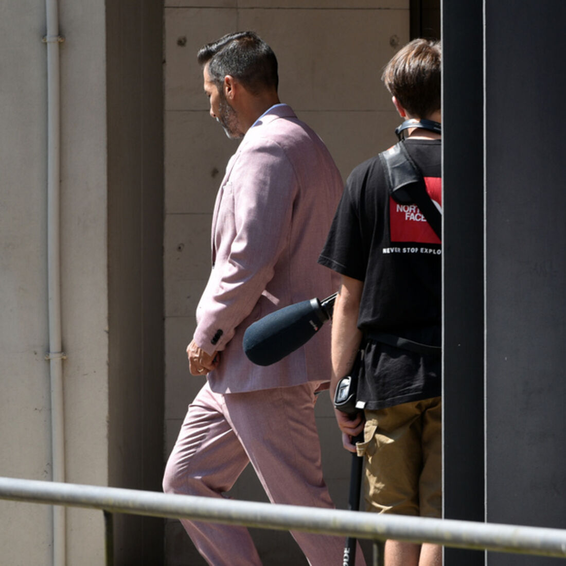 Homem de fato rosa caminha com equipa de filmagem