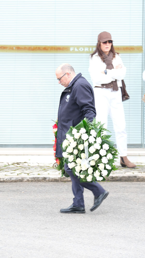 Homem carrega coroa de flores, com pessoas em frente a loja 'Florista'