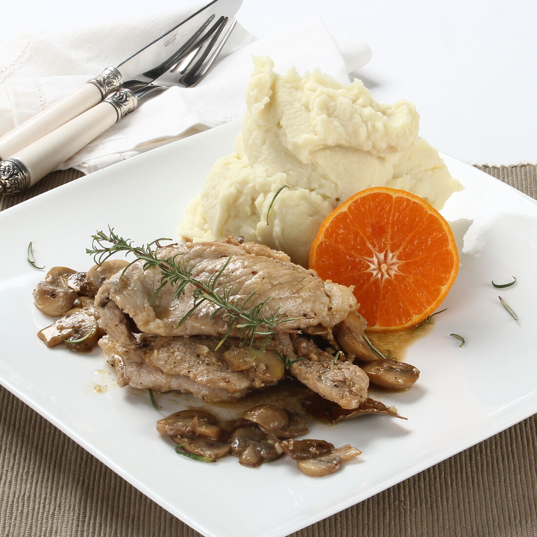 Escalopes de porco com cogumelos, puré de batata e laranja numa travessa