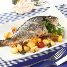 Dourada assada com batatas e legumes, servida num prato branco