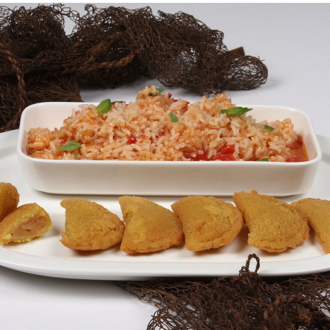Rissóis de peixe dourados acompanham arroz de tomate, numa apresentação tradicional