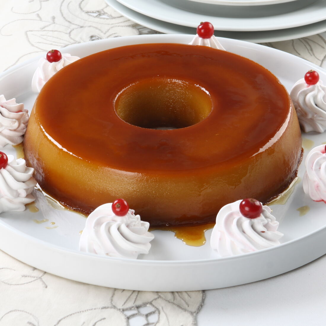 Pudim Abade de Priscos decorado com chantilly e groselhas numa mesa