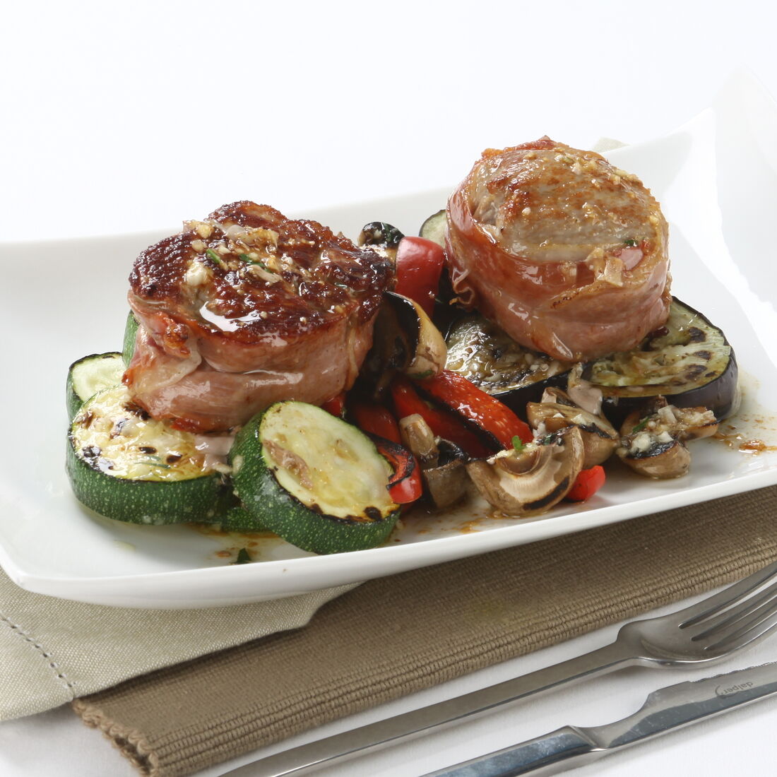 Medalhões de vitela com legumes grelhados num prato branco