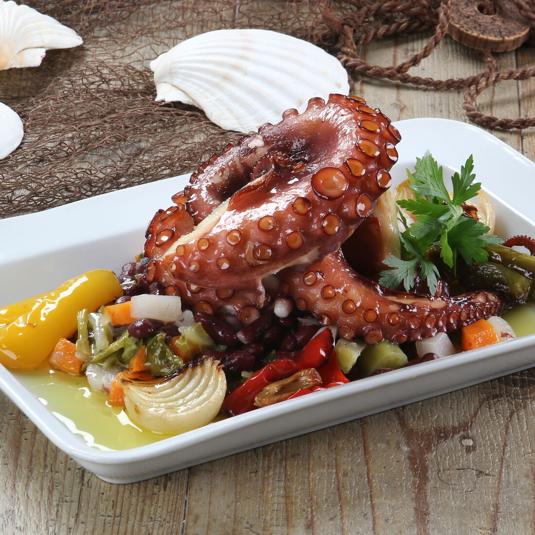 Polvo assado com legumes, apresentado num prato branco com decoração marítima