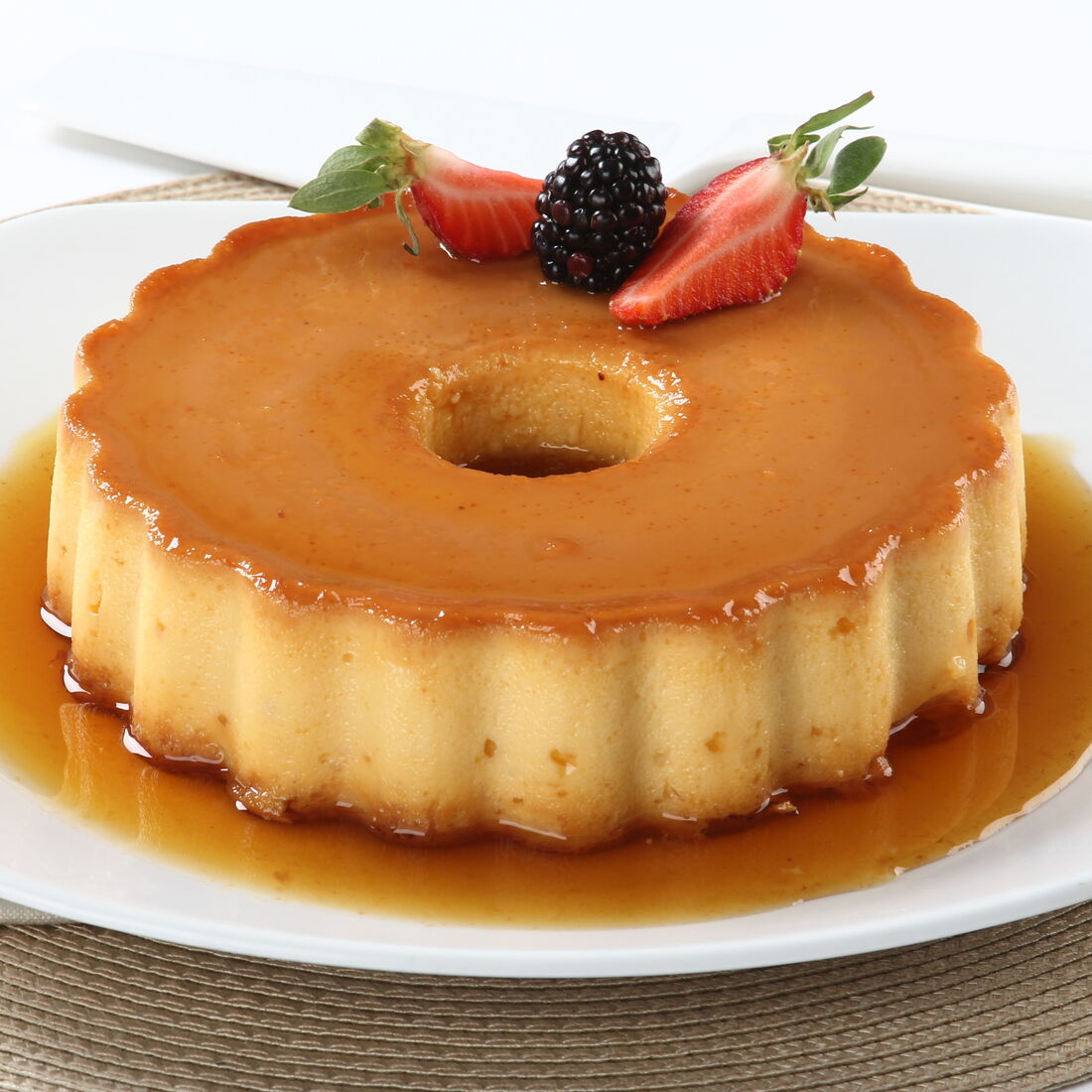 Pudim de leite condensado decorado com morangos e amoras numa travessa branca