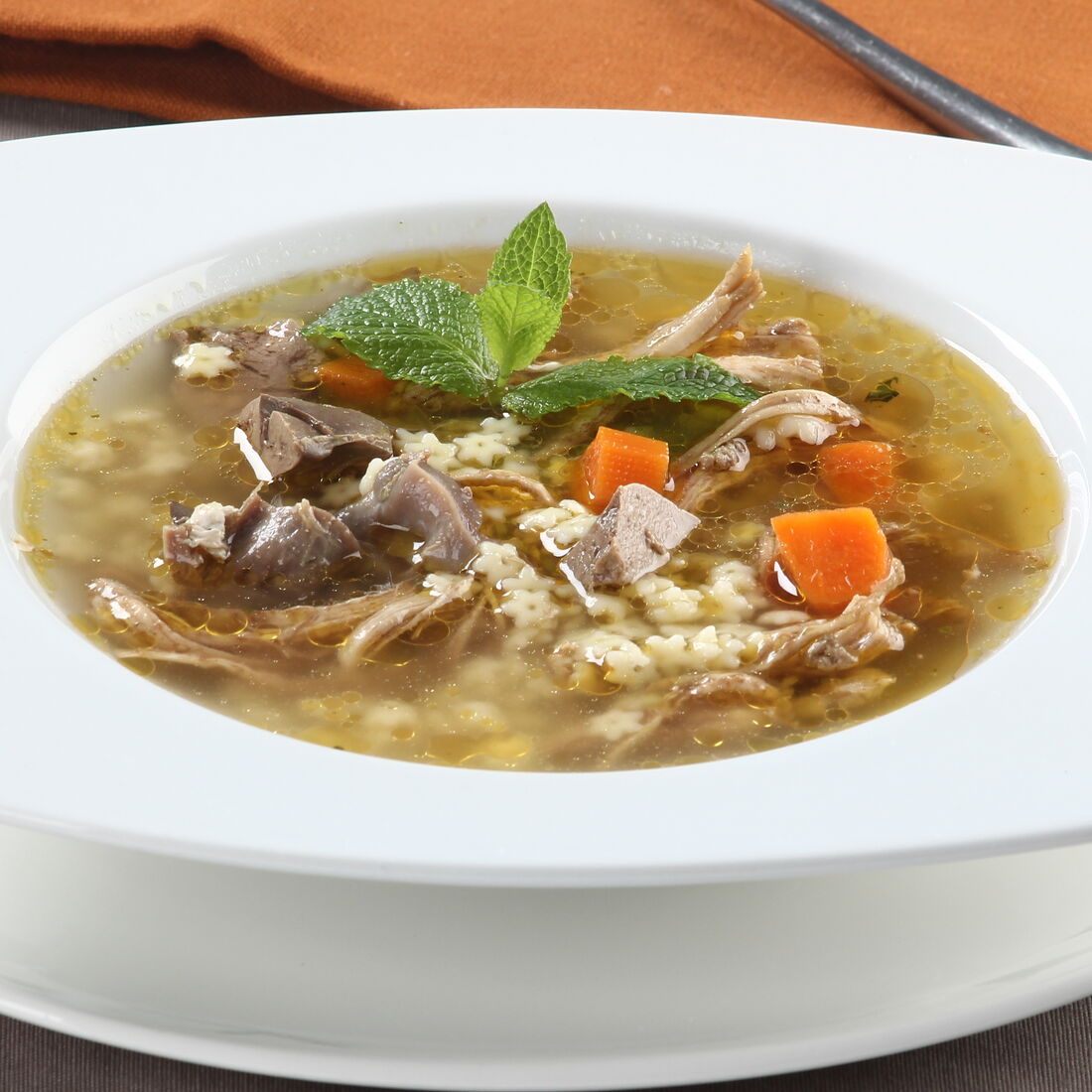 Canja de pato com massa, cenoura e hortelã numa taça branca