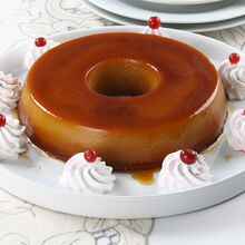 Pudim Abade de Priscos decorado com chantilly e groselhas numa mesa