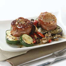 Medalhões de vitela com legumes grelhados num prato branco