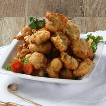 Prato de sonhos de alheira frita com tomate e decoração de ervas