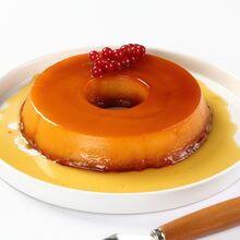 Pudim de gemas com calda e decoração de groselhas numa travessa com espátula