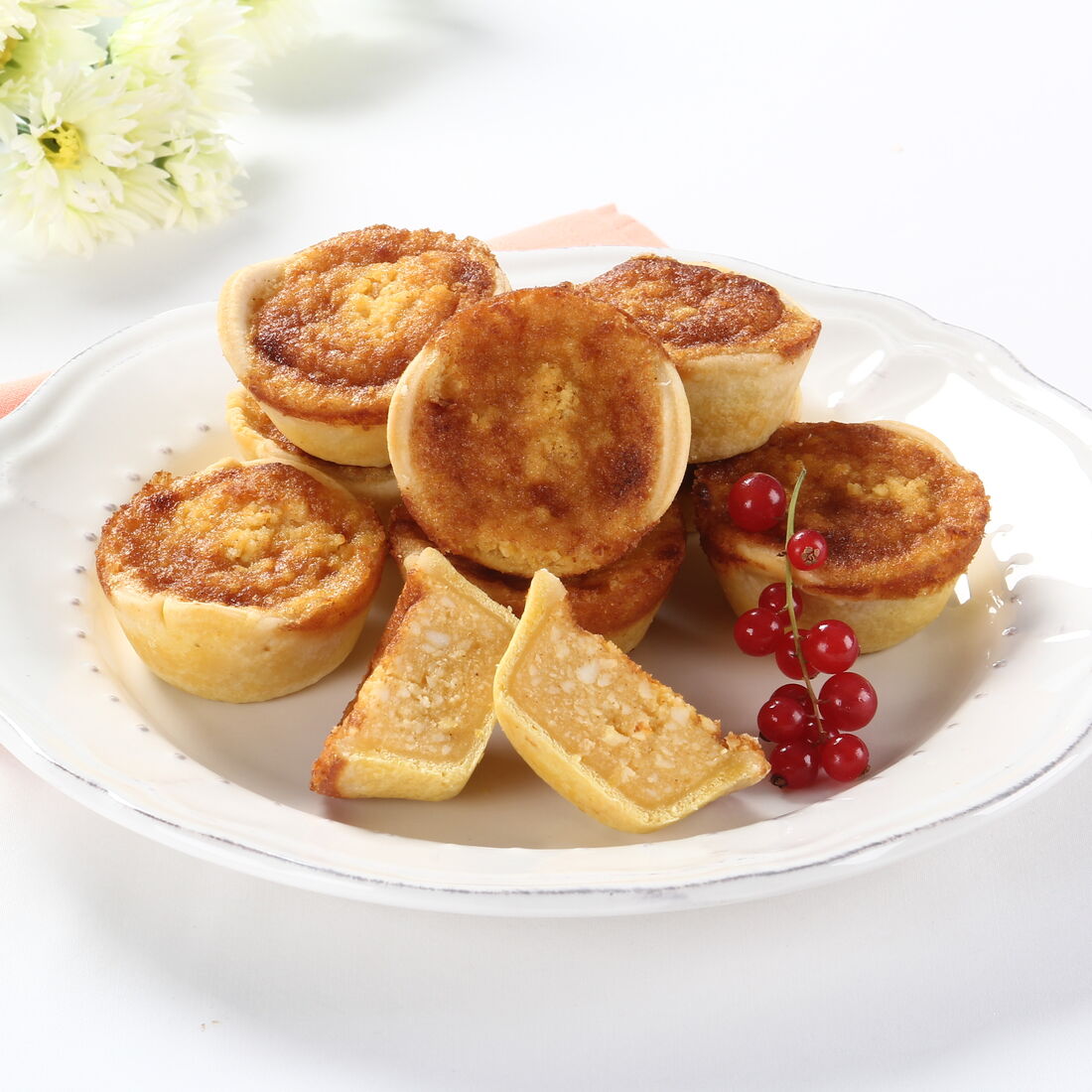 Queijadas de requeijão em prato branco com flores e um pano