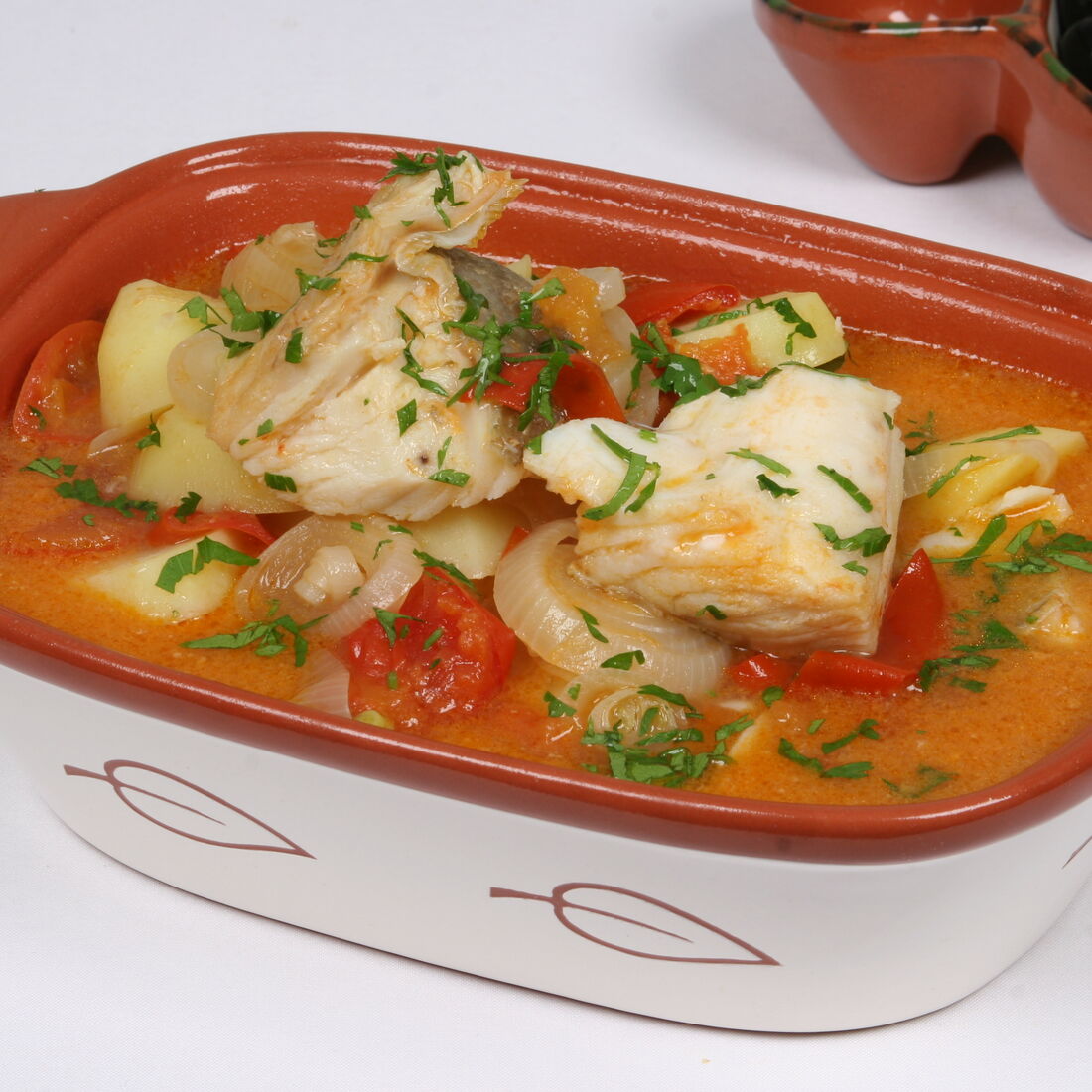 Bacalhau guisado com batatas, tomate e cebola num recipiente de barro