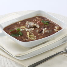 Sopa da Pedra num recipiente branco, com colher ao lado