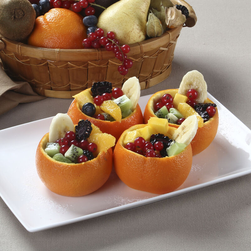 Cesto de frutas com variedade e tacinhas de laranja recheadas com salada de fruta
