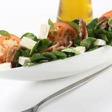 Salada de anchovas com tomate e queijo feta, servida numa travessa branca com azeite