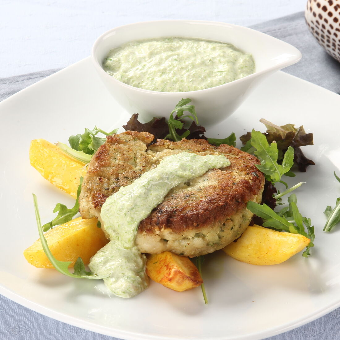 Hambúrguer de peixe com molho e batatas no prato