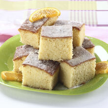 Bolo de laranja com açúcar e rodelas de laranja numa travessa verde