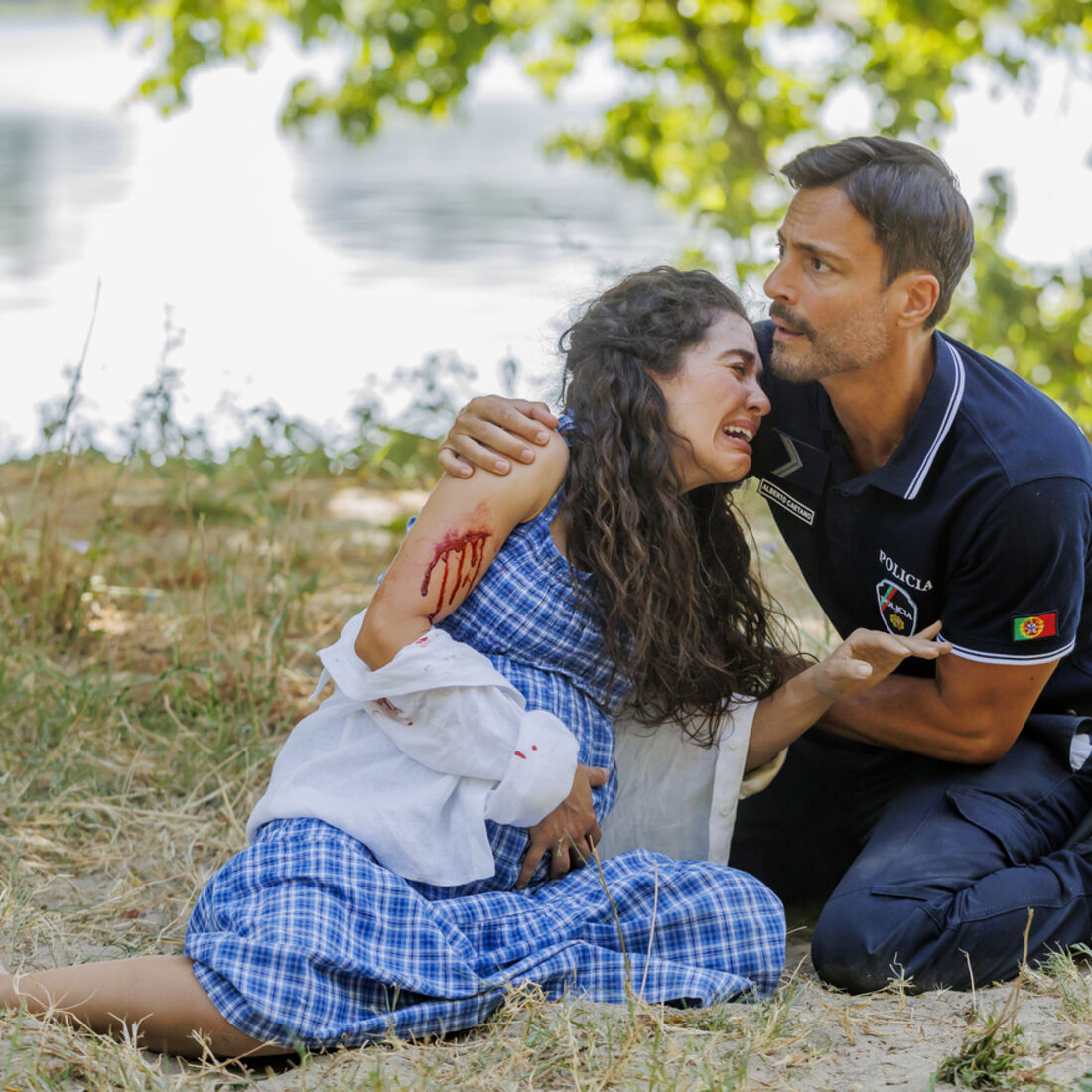 Uma mulher grávida ferida é consolada por um polícia junto a um lago
