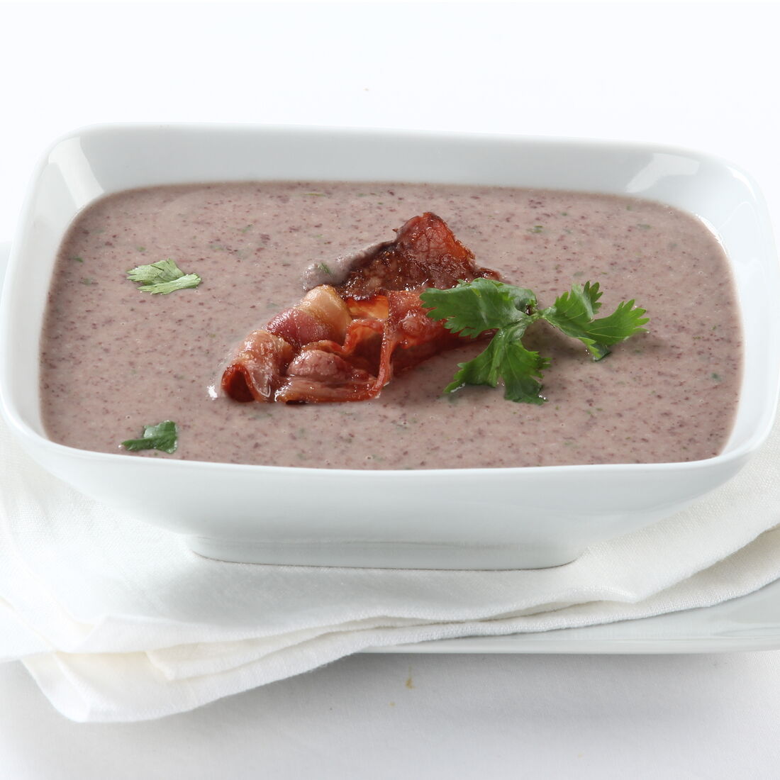 Creme de feijão encarnado com bacon e salsa numa taça branca